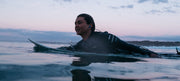 Leo on a surfboard in glassy water in evening purple light