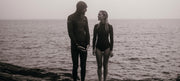 Nick and Sarah standing in wetsuits in front of the sea